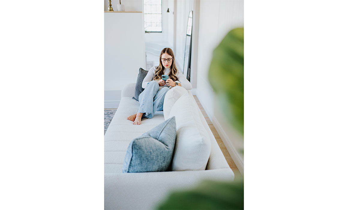 teenager texting on a white channel tufted sofa