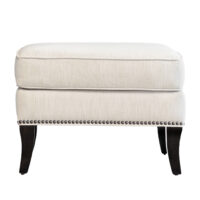 Straight-on shot of the Atticus Ottoman by Vogel with wooden legs, cream fabric, and nailhead trim